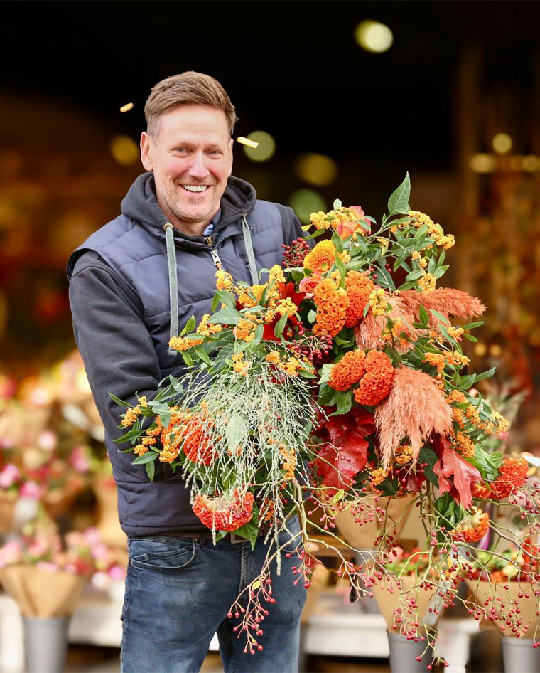 Man met een groot boeket oranje en rode herfstbloemen op een markt.