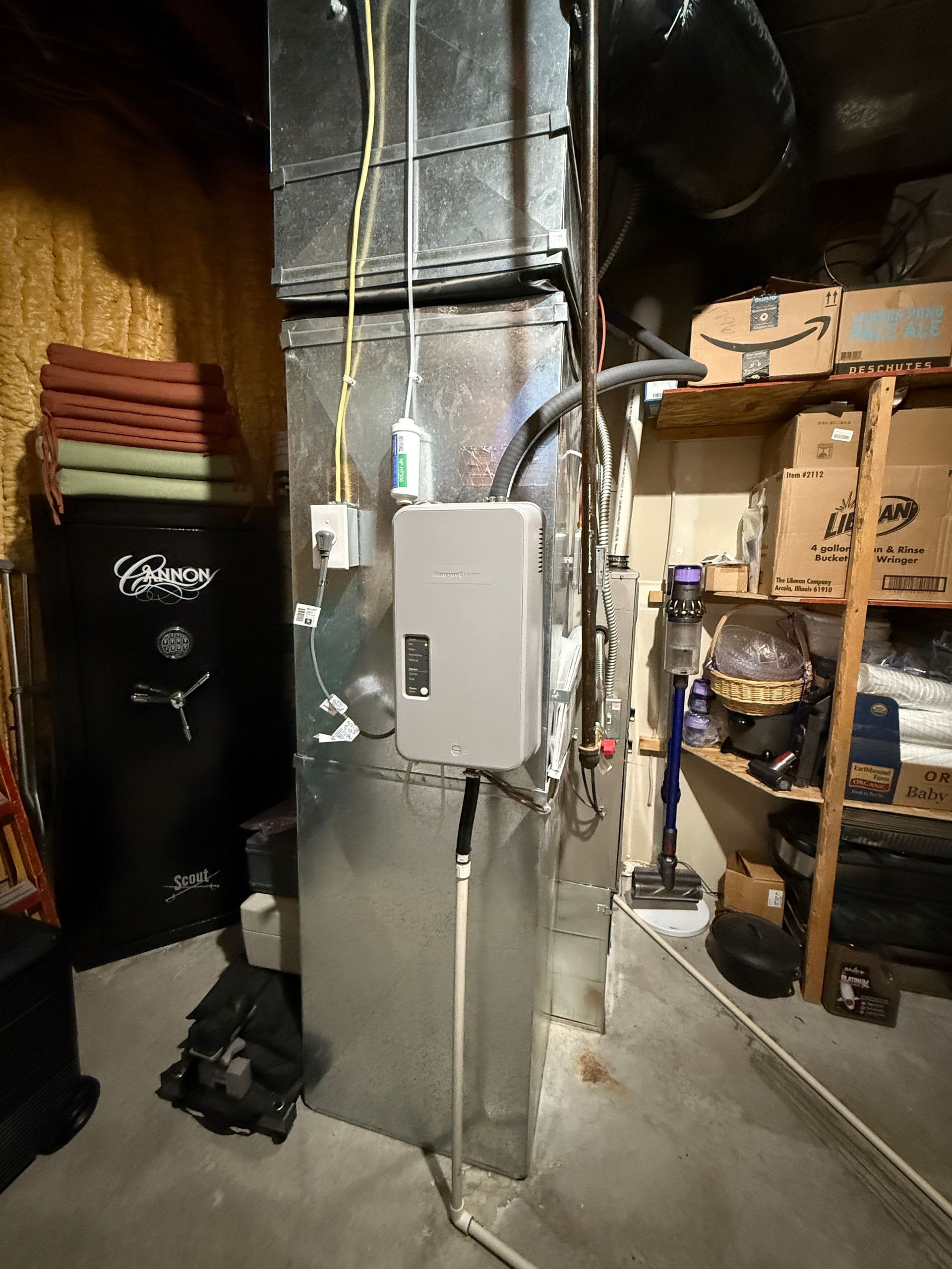 Basement utility area with HVAC ducts, breaker panel, storage shelves, and a black trash bin.