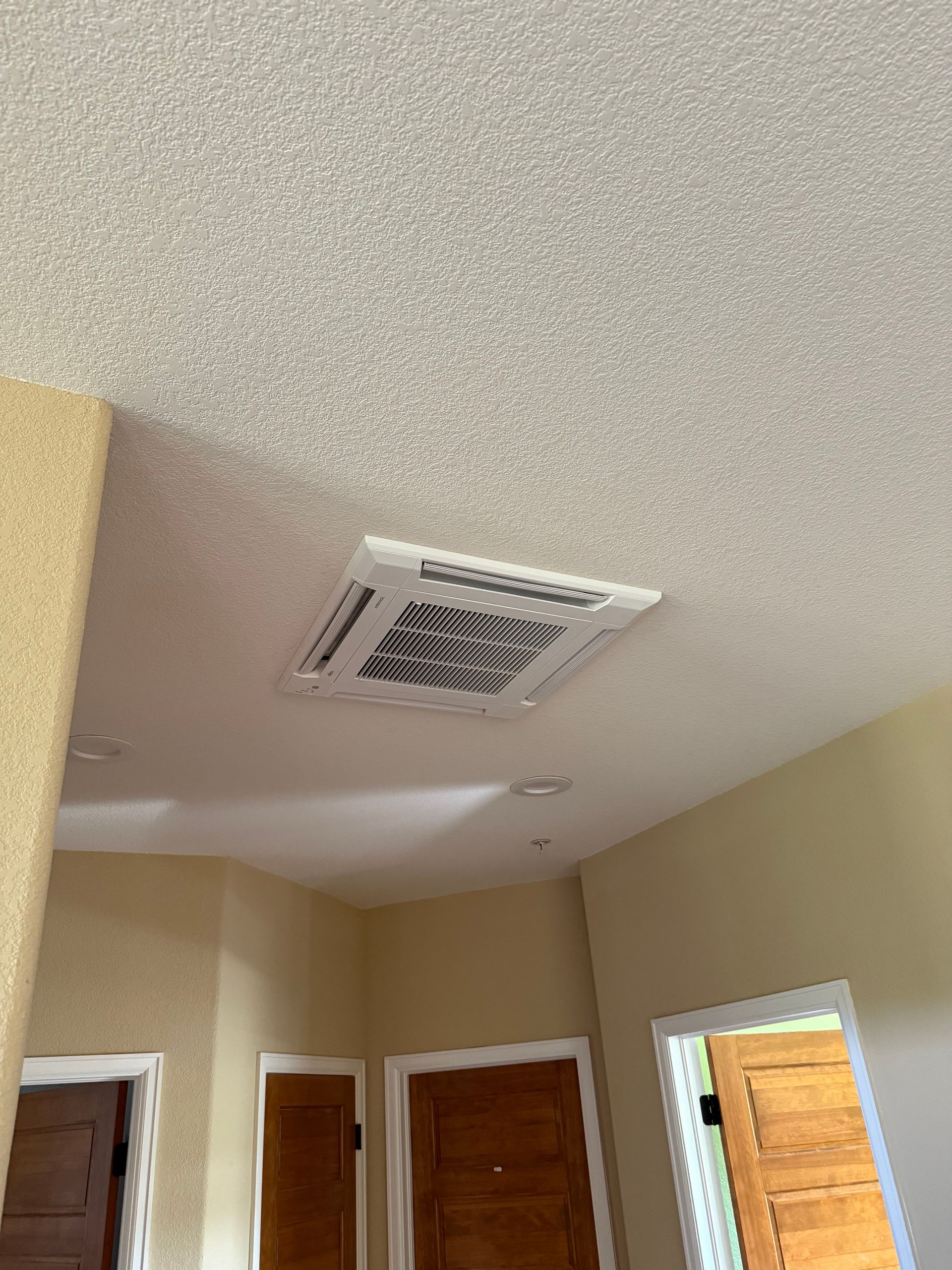 Ceiling vent in a beige hallway with white trim and wooden doors.