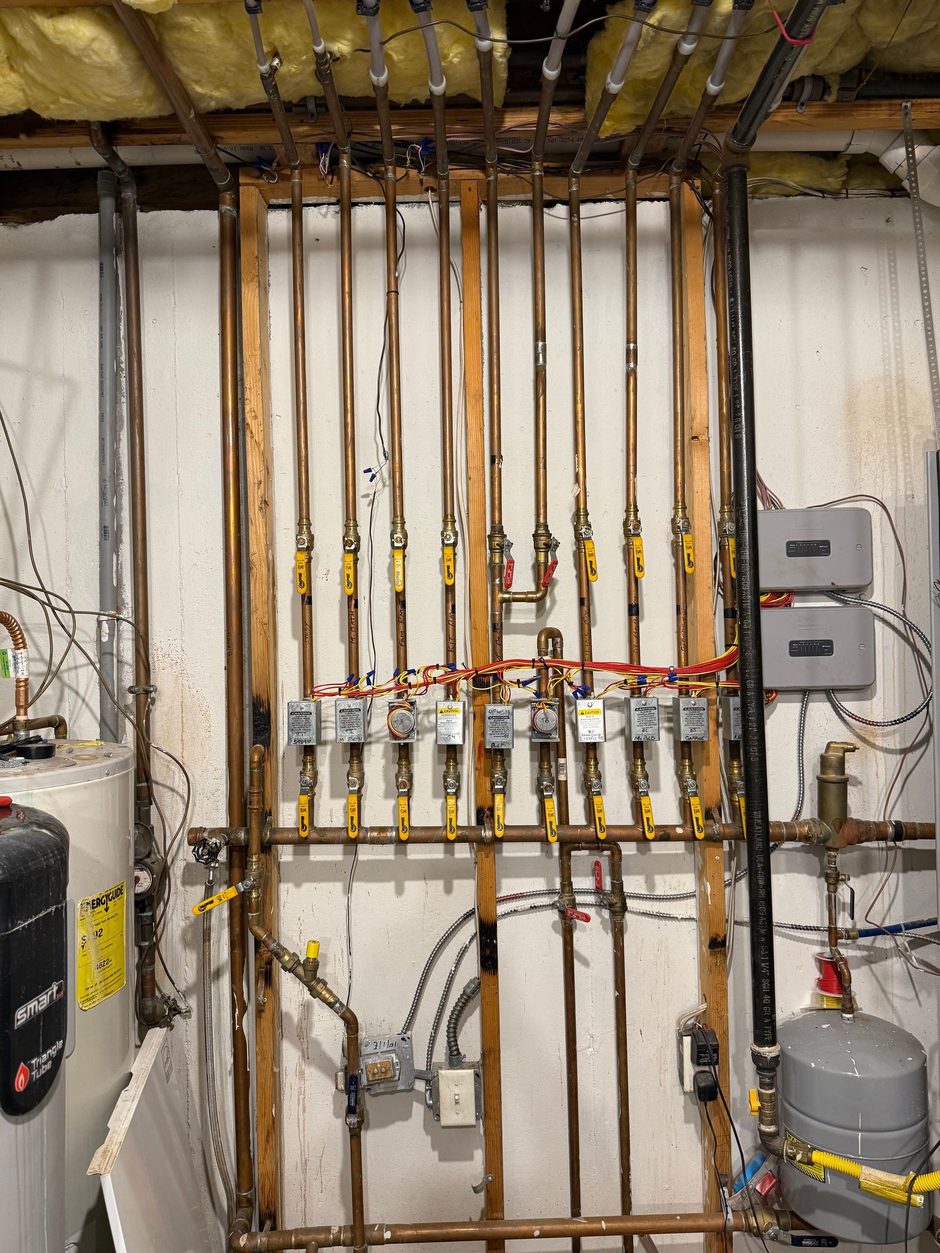 Rows of copper pipes and gas valves in a utility room with wall-mounted meters and tanks.