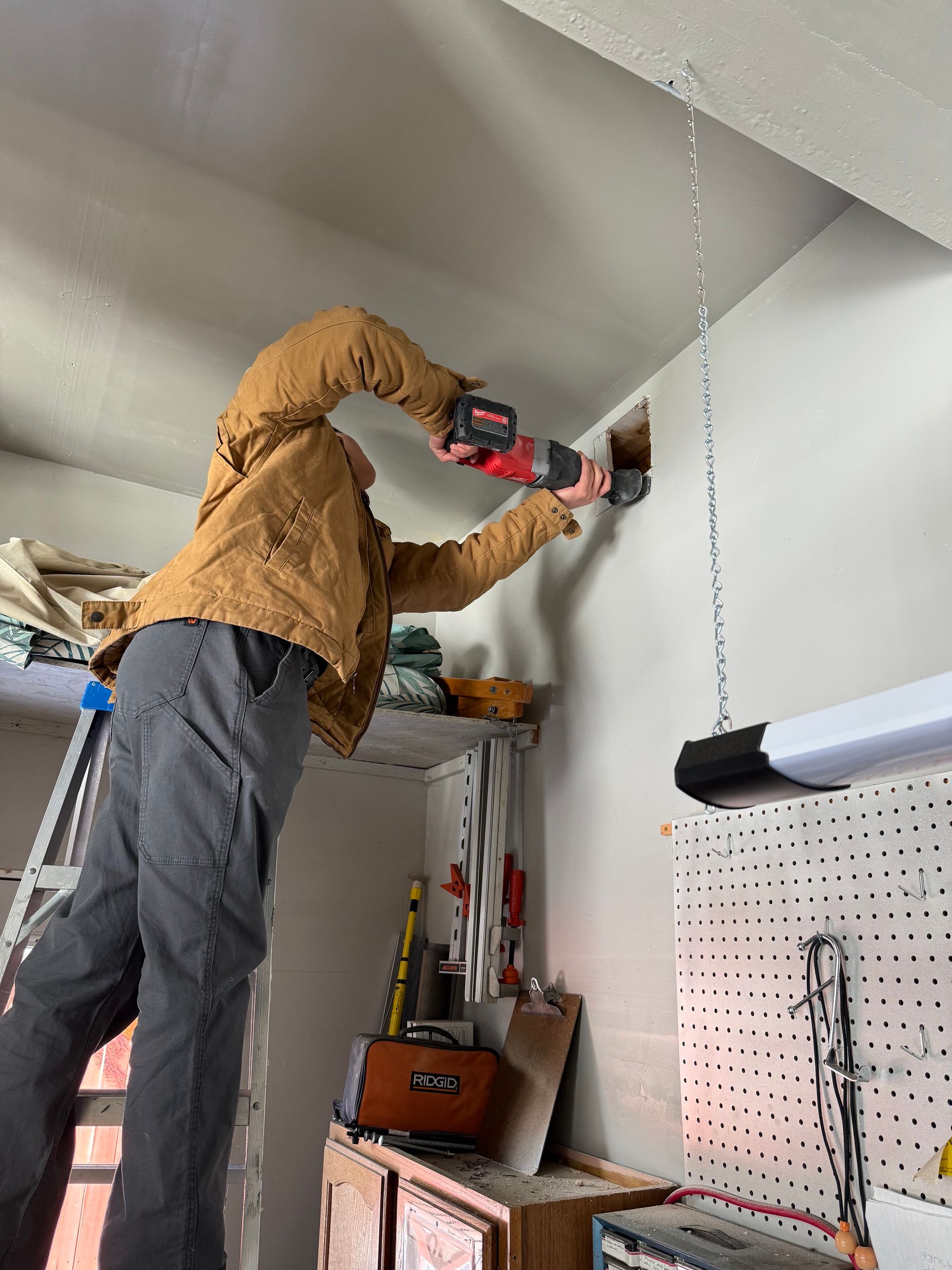 Person using a red power drill to work on a wall in a garage or workshop