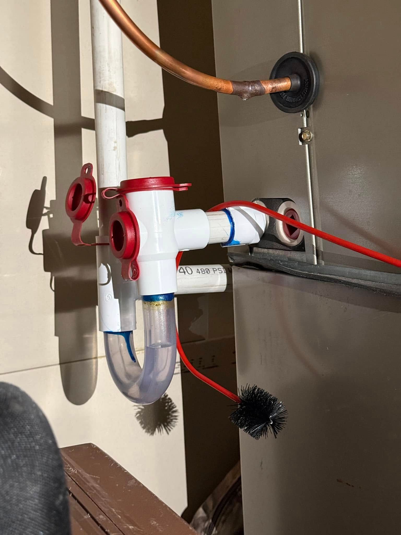Under-sink plumbing with red and white PVC pipes, a clear trap, and a drain line inside a cabinet.