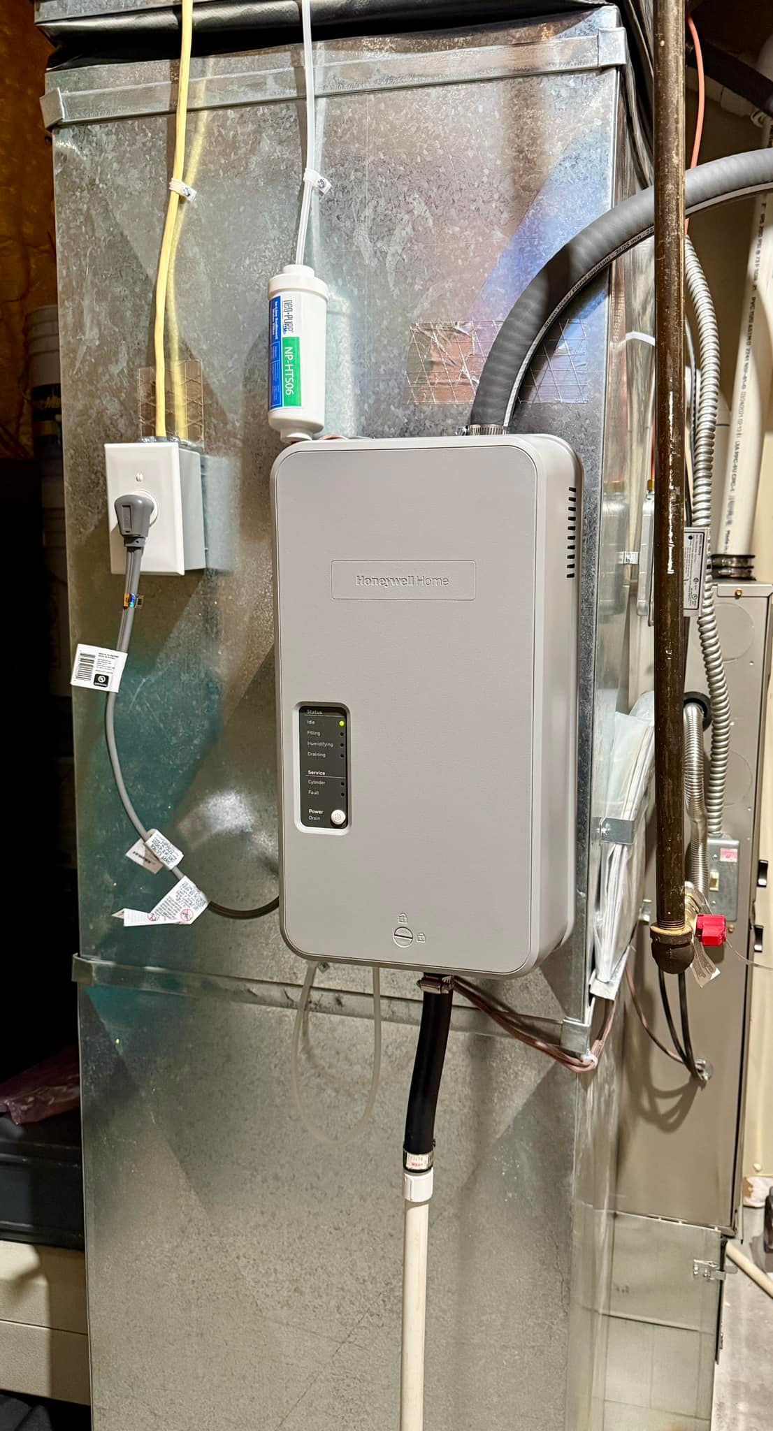 Gray electrical control panel mounted on a basement wall beside pipes and cables