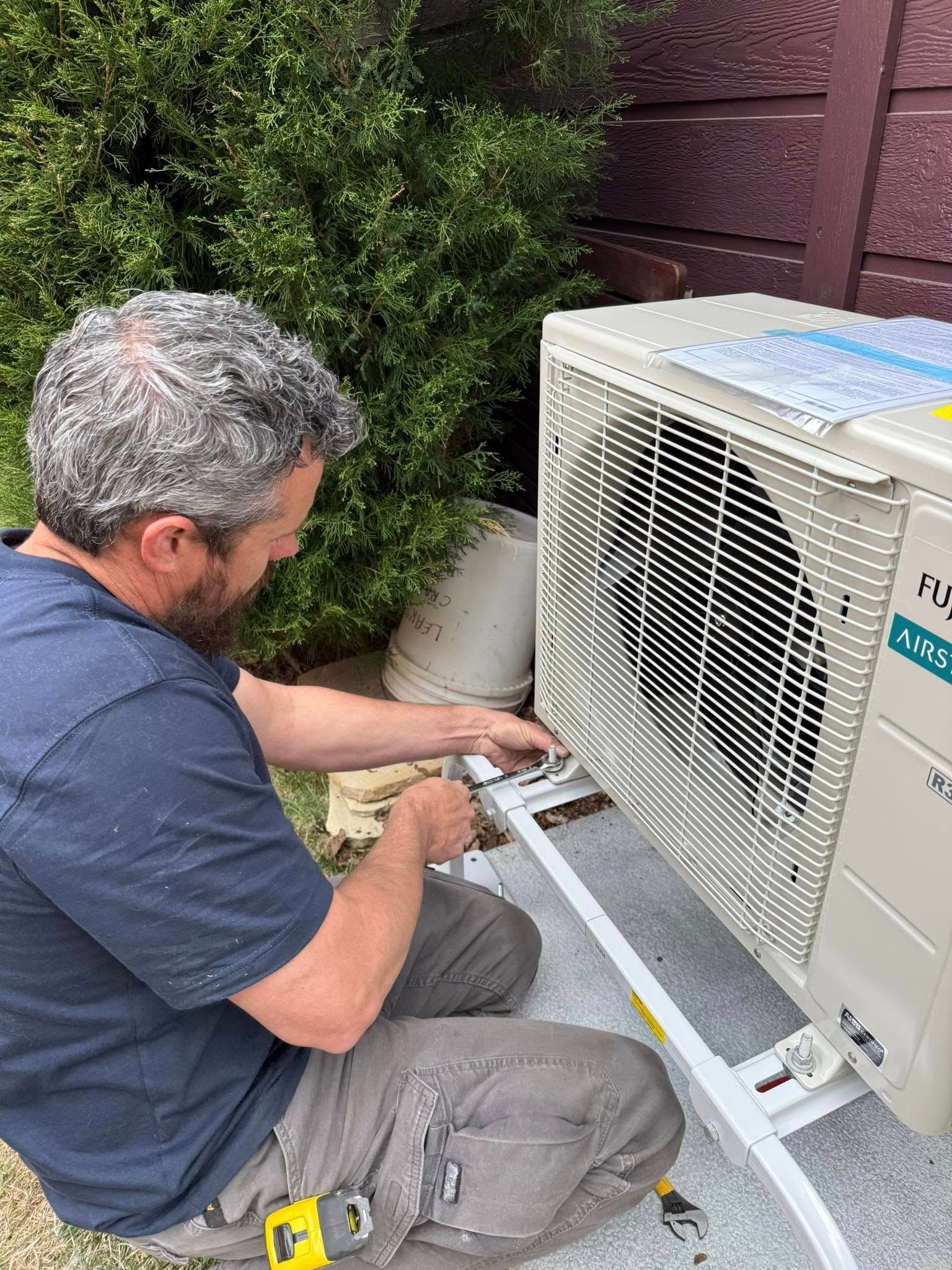 Technician kneels beside an outdoor AC unit, adjusting wiring on a rooftop or patio.