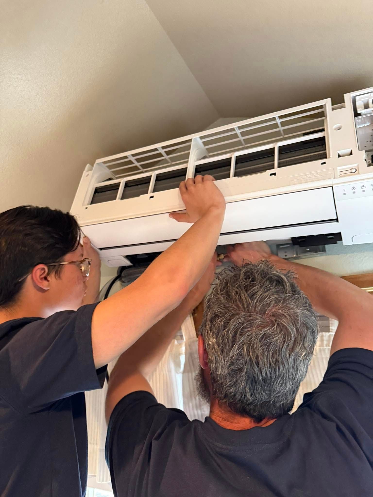 Two men adjusting a wall-mounted air conditioner filter indoors