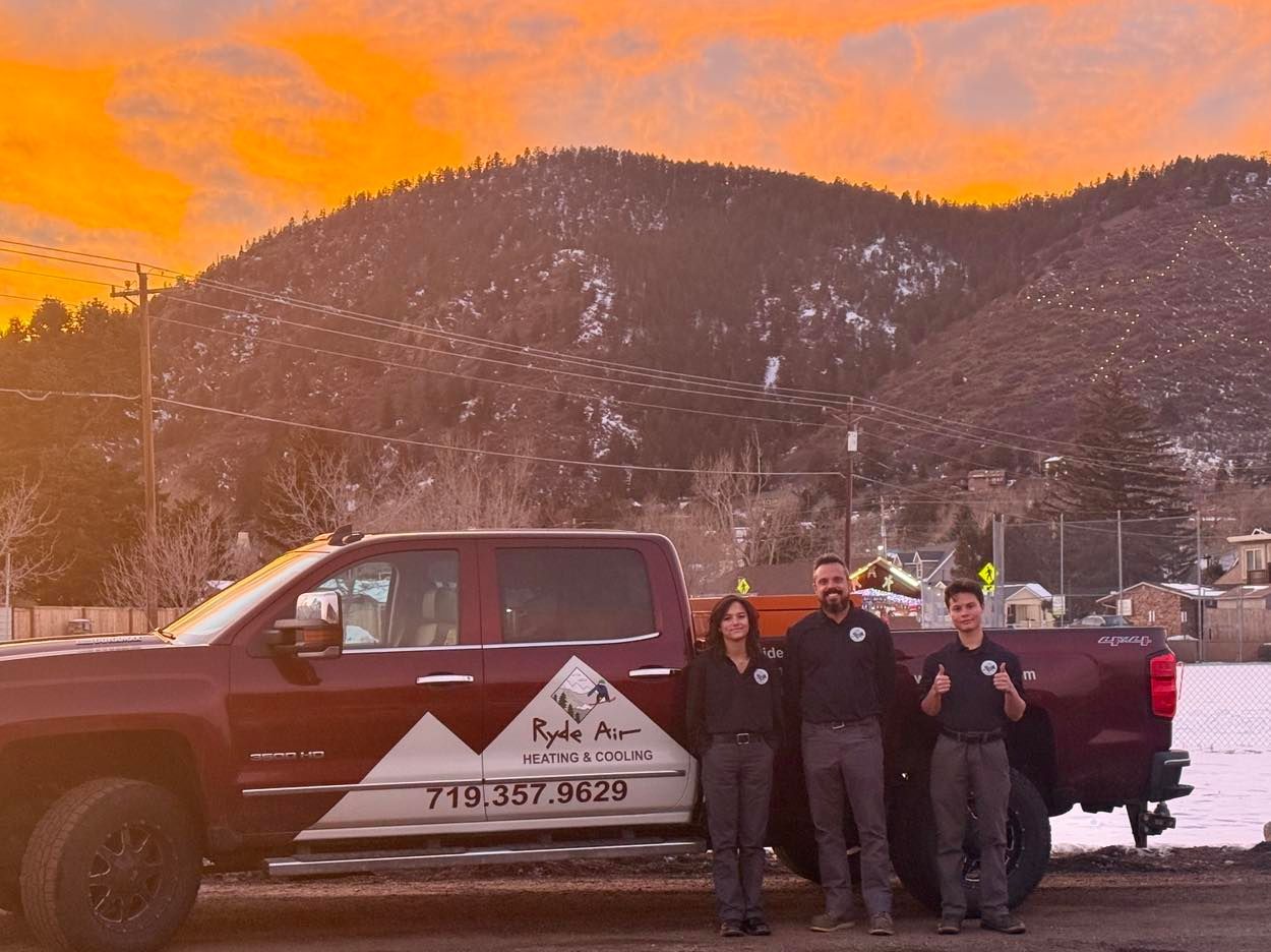 People posing beside a maroon pickup truck in a snowy mountain setting at sunset.