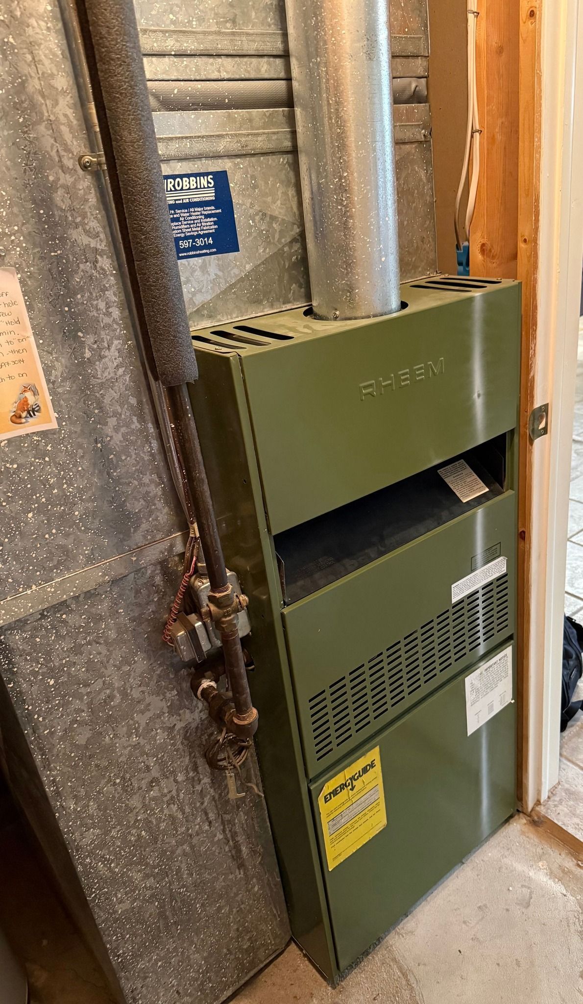 Green HVAC furnace in a narrow utility closet with exposed ductwork and insulated walls