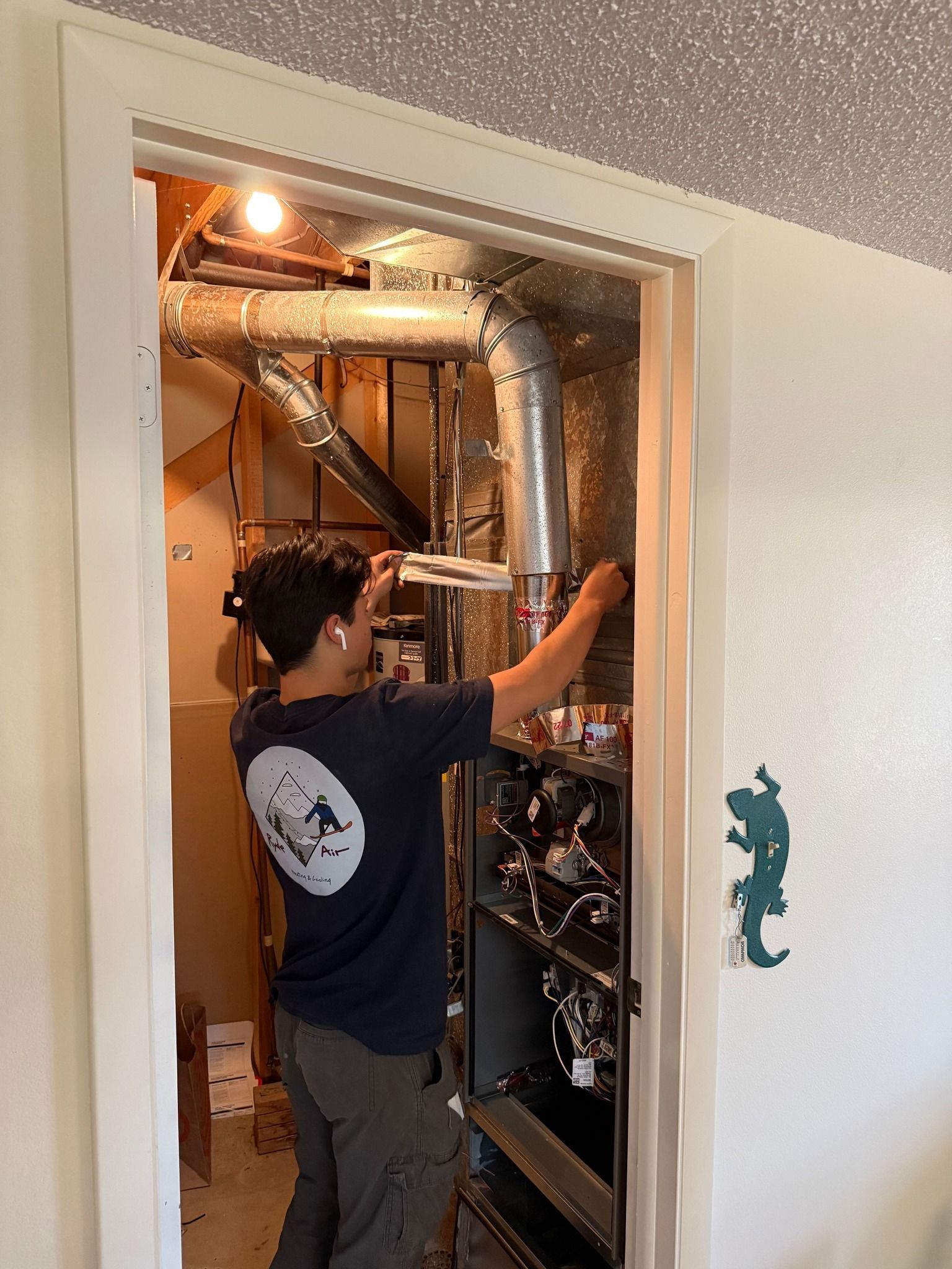 Person inspecting HVAC equipment inside a closet, with exposed ductwork and pipes.