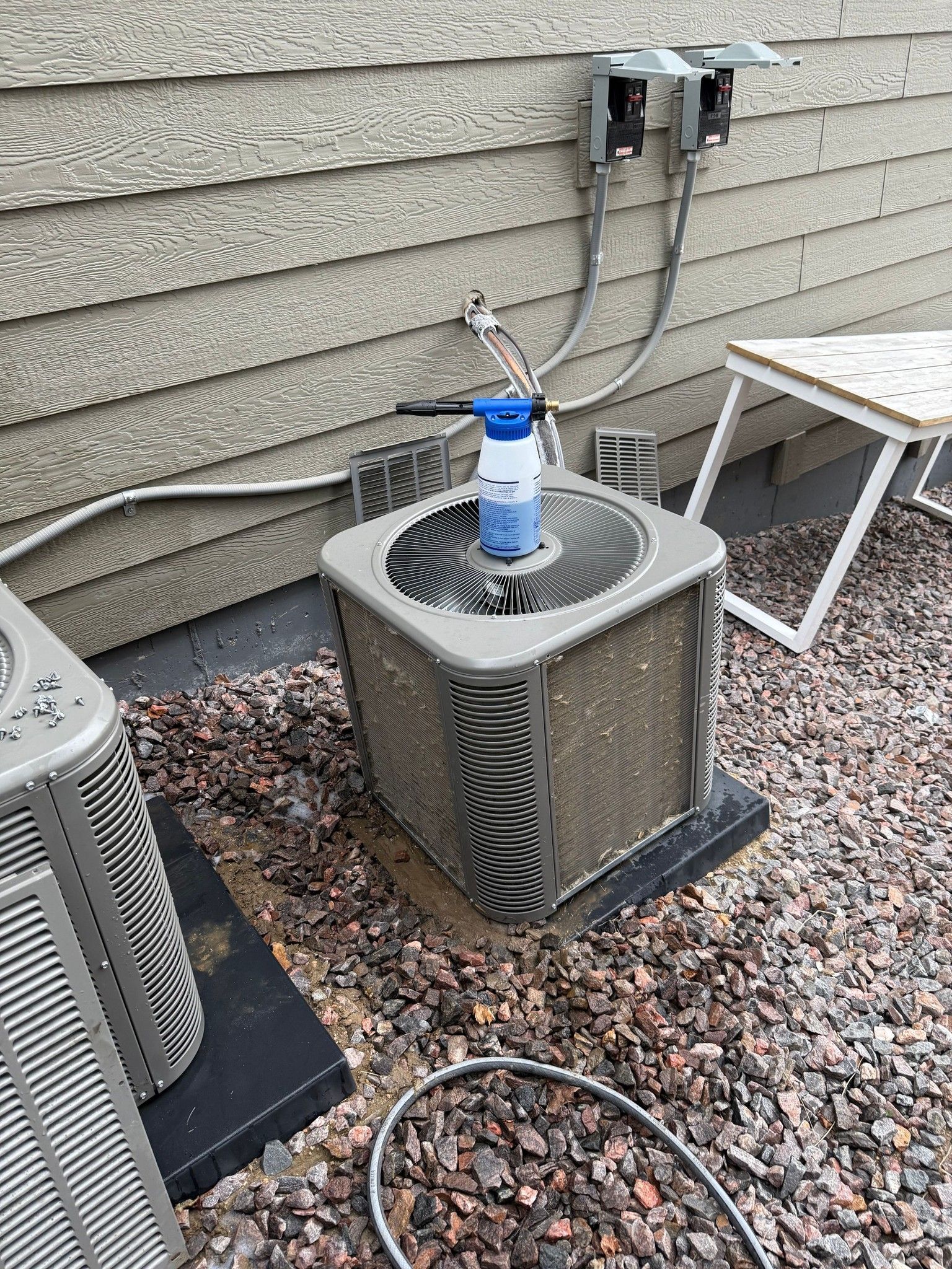 Outdoor air-conditioning units beside a house wall, with a water bottle on top of one unit.