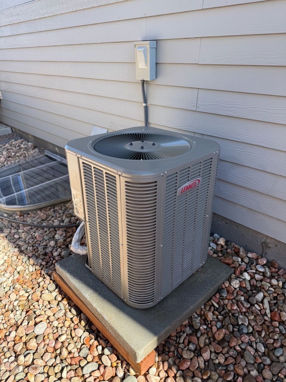 Outdoor air conditioner unit beside a house wall on a gravel bed