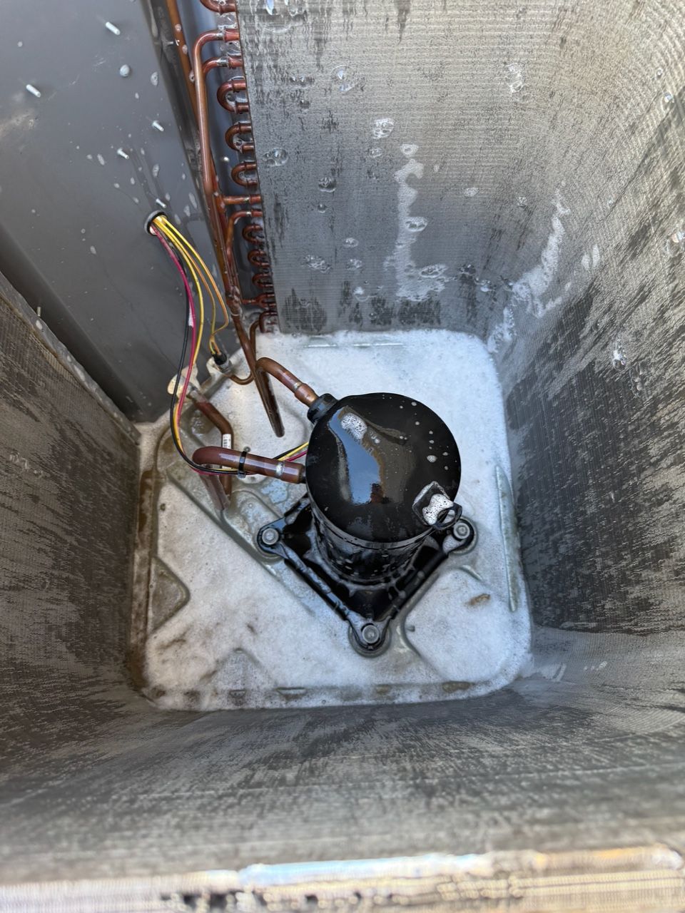 Inside a metal chamber, a black pump sits in white liquid with exposed wires and tubing.