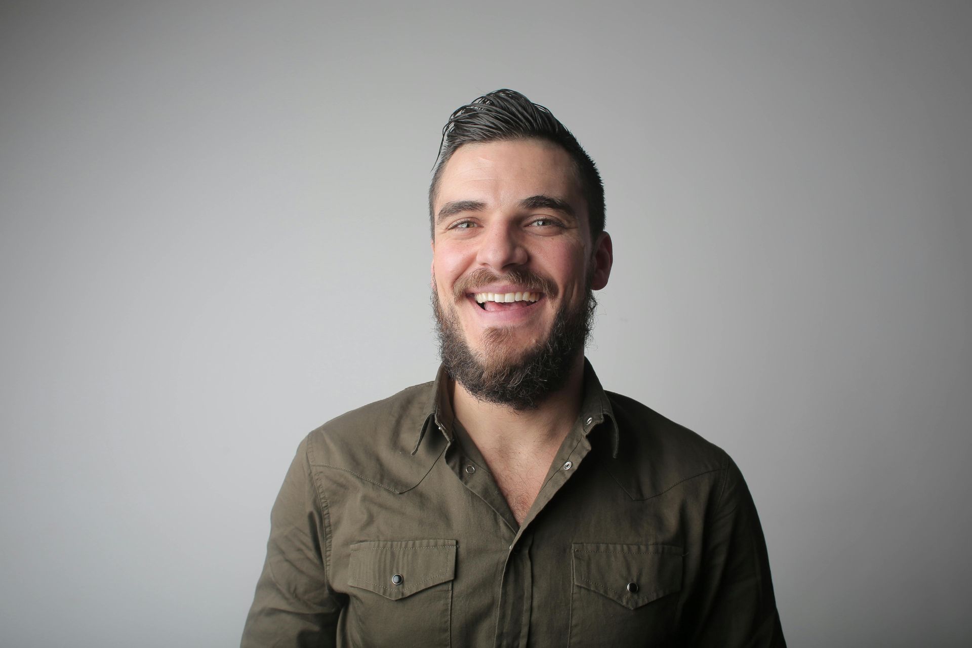 Smiling man with a beard in an olive shirt against a light gray background