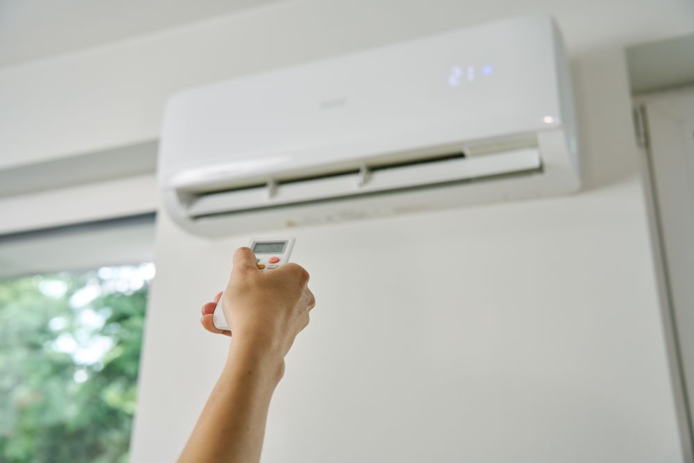 A Person Is Turning on An Air Conditioner — Gympie Air-Conditioning & Refrigeration In Southside, QLD