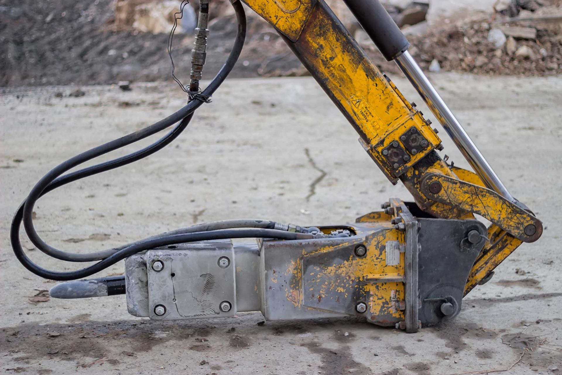 Excavator hydraulic hammer at construction site showing wear from heavy-duty industrial use.