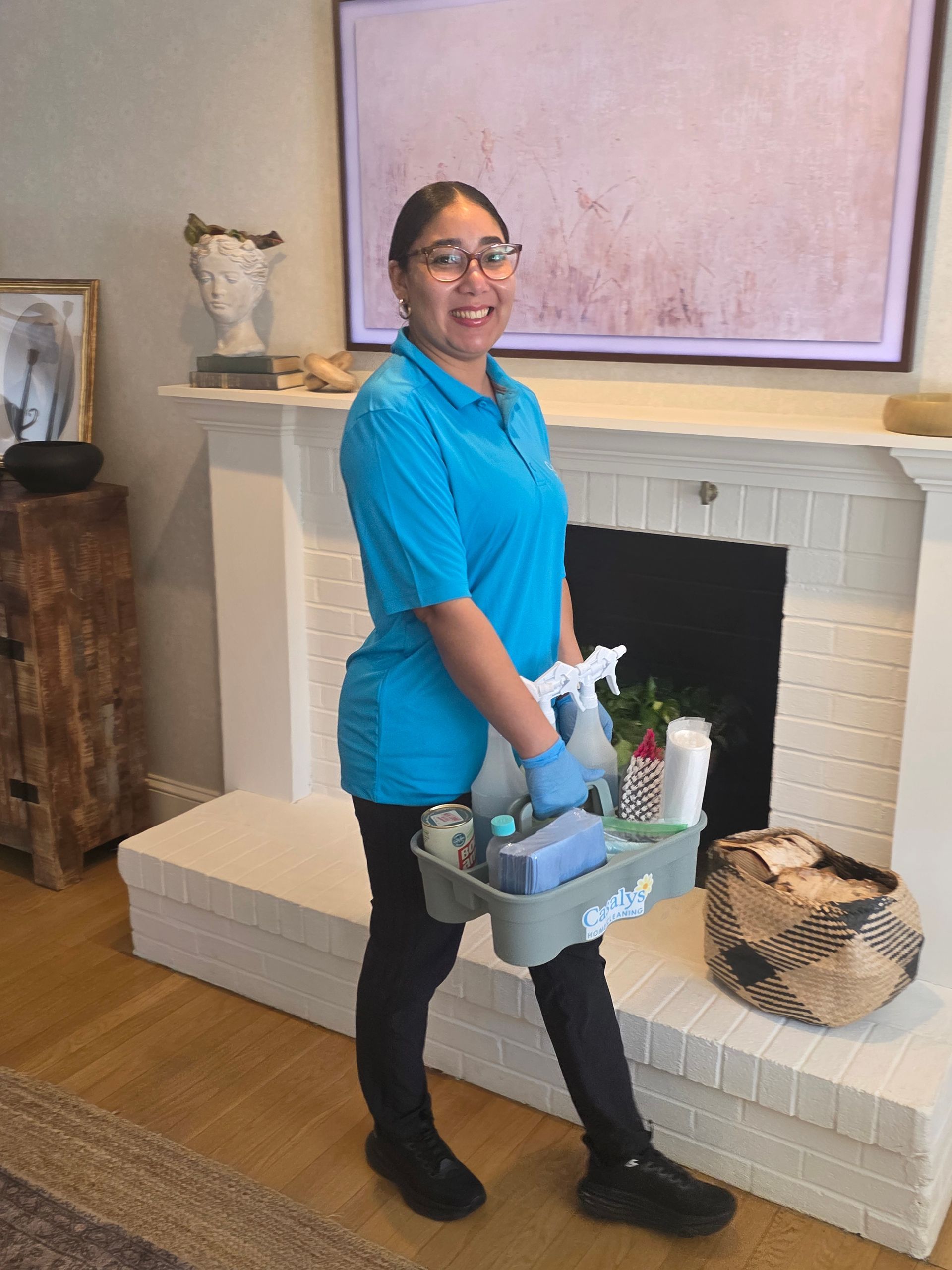 Person in blue shirt and black pants holding a cleaning caddy beside a white fireplace in a living room.
