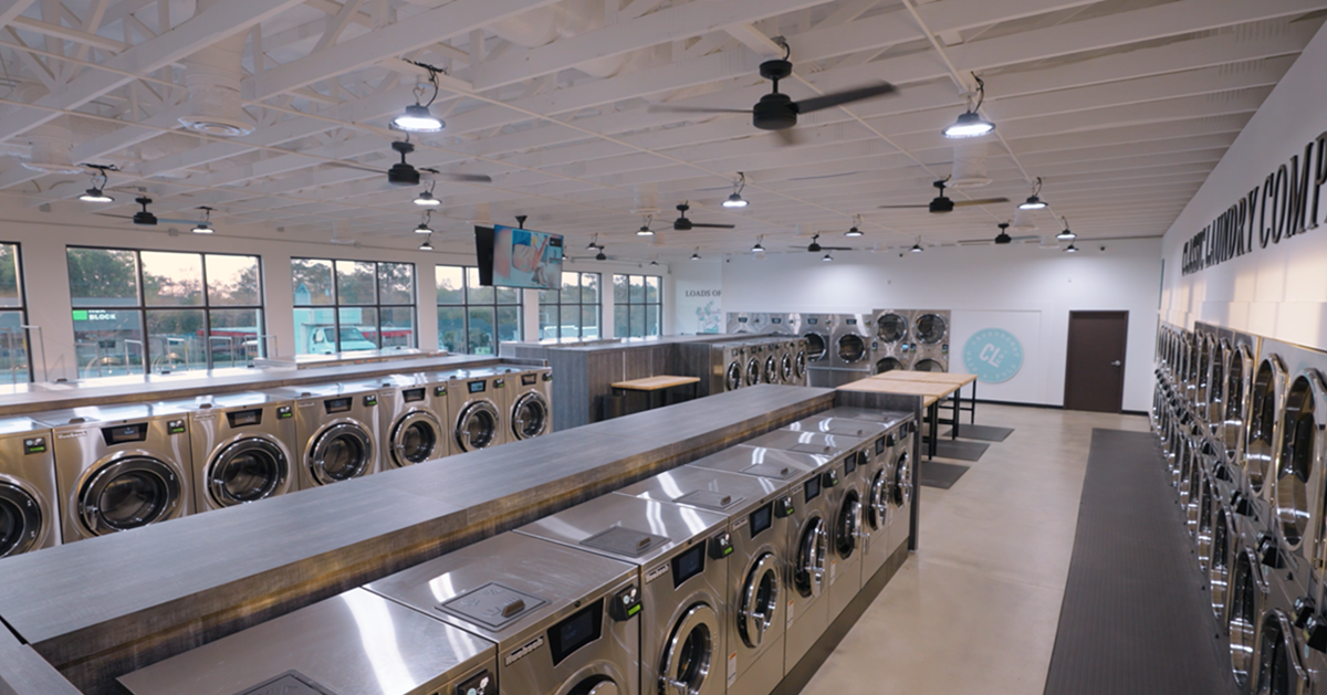 Row of commercial washing machines and dryers inside Classic Laundry Company.