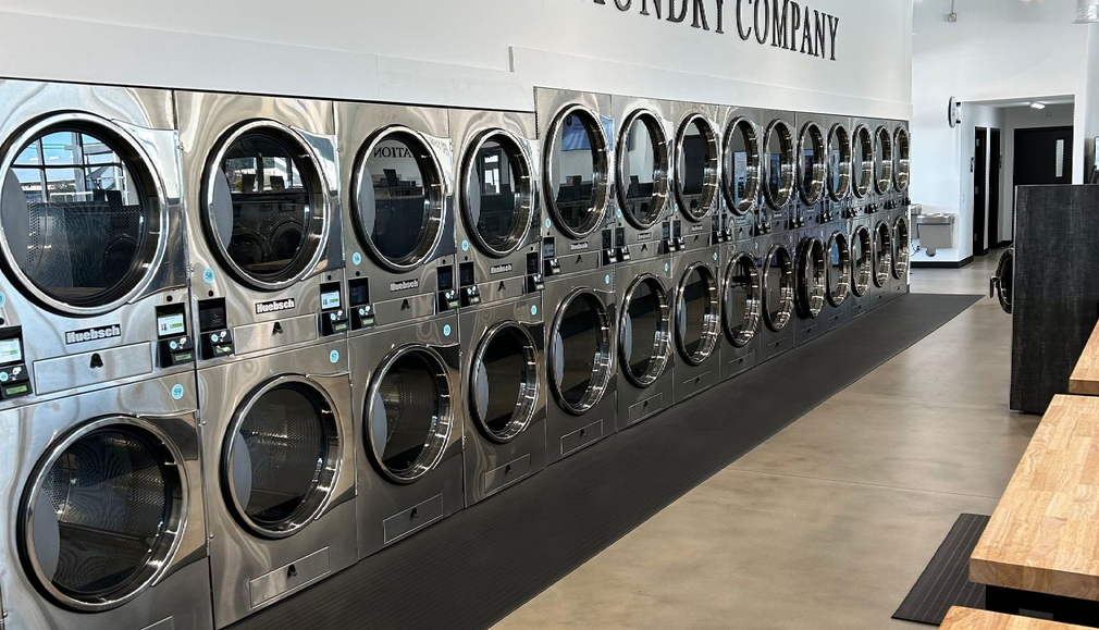 Row of commercial washing machines and dryers inside Classic Laundry Company.