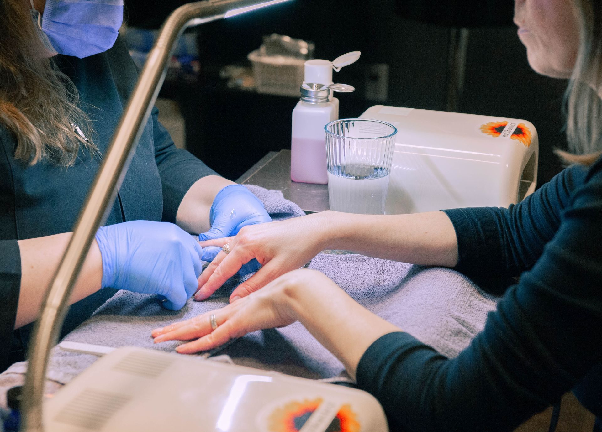 A woman is getting her nails painted by a nail artist wearing black gloves.