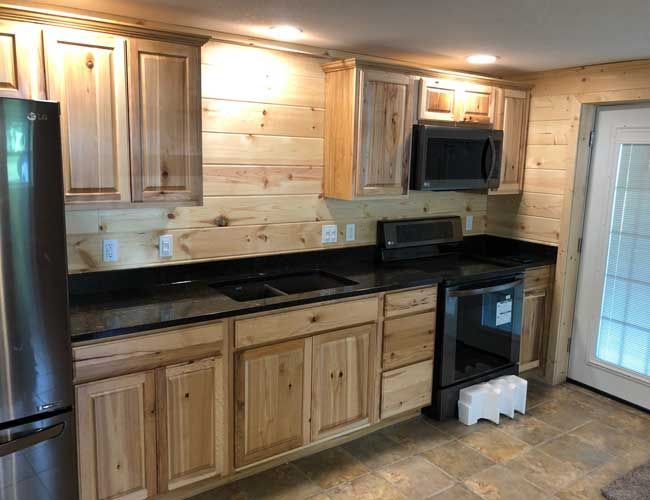 Wood-paneled kitchen with stainless steel fridge, black countertops, and a wall-mounted microwave.