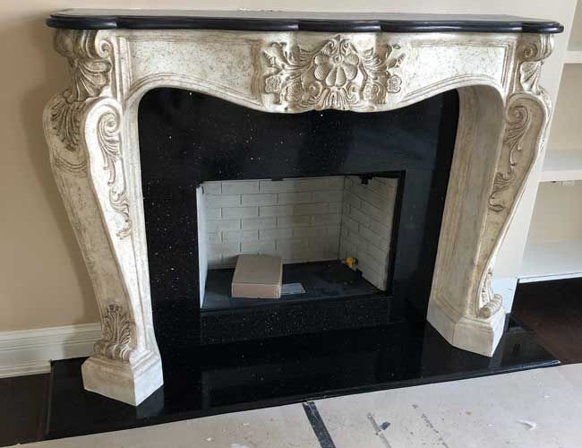 Ornate cream fireplace with black surround and white tiled firebox on a dark floor.