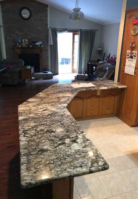 Kitchen with a dark granite peninsula extending into a living room, tiled floor, and sliding door to a patio.