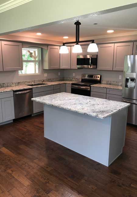 Modern kitchen with white granite island, gray cabinets, stainless appliances, and dark hardwood floors
