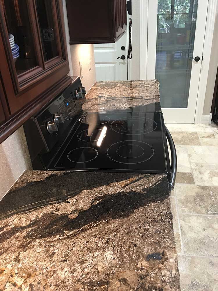 Granite kitchen countertop with a black electric cooktop and dark wood cabinets by a glass door