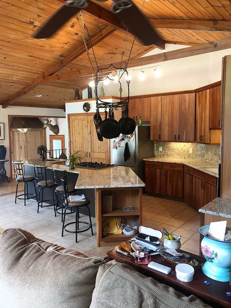 Kitchen with wood ceiling, granite island, black chairs, and wooden cabinets in a cozy open-plan home