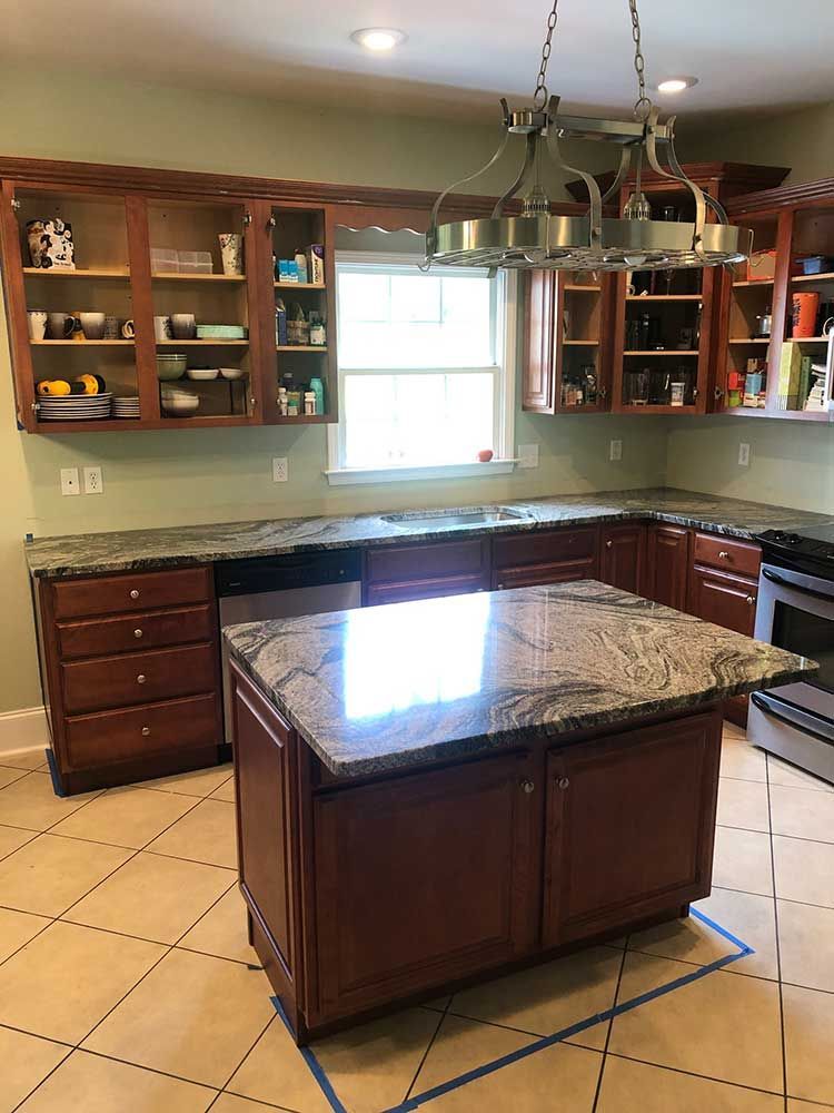 Kitchen with dark wood cabinets, granite island, tile floor, and large window over the sink.
