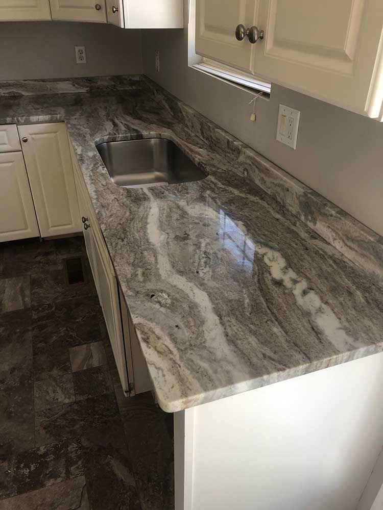 Kitchen countertop with gray marbled granite, stainless sink, and beige cabinets