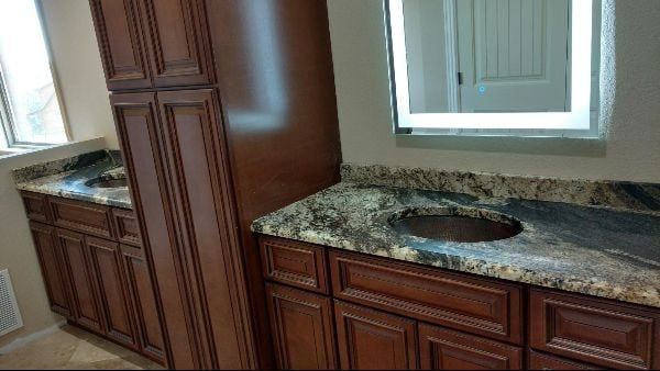 Bathroom vanity with dark wood cabinets, marble countertop, sink, and a large mirror near a window.