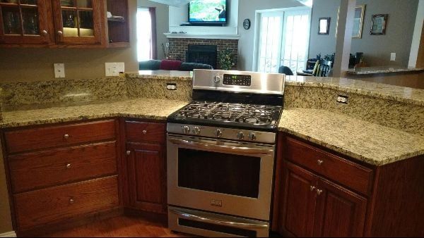 Modern kitchen with granite countertops, wood cabinets, and stainless steel stove and oven.