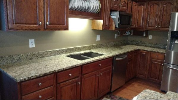 Kitchen with dark wood cabinets, granite countertop, stainless sink, and tiled floor.