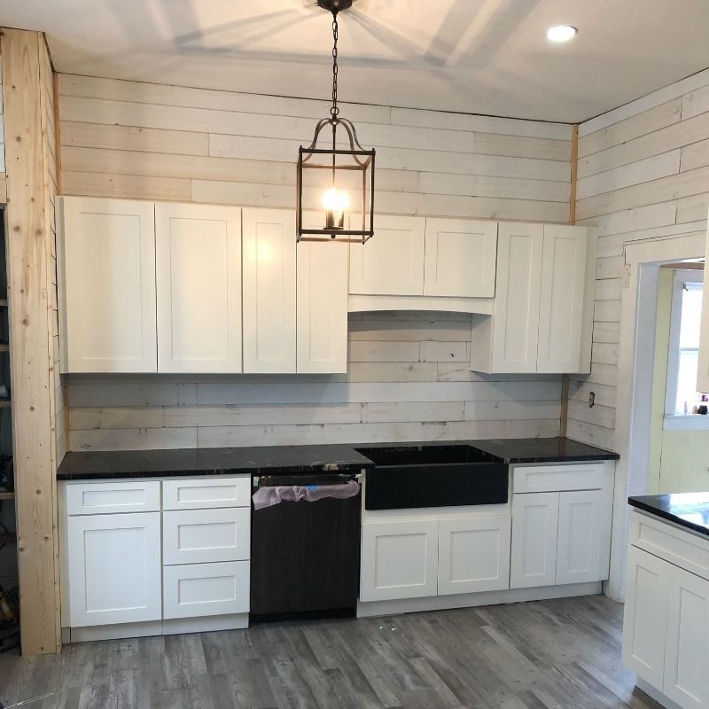 Modern white kitchen with black countertops, gray wood floor, and hanging pendant light