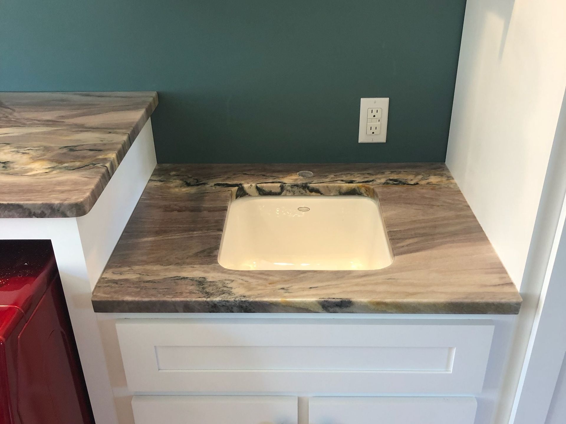 Kitchen counter with beige sink, wood-look countertop, teal wall, and white cabinet drawer.