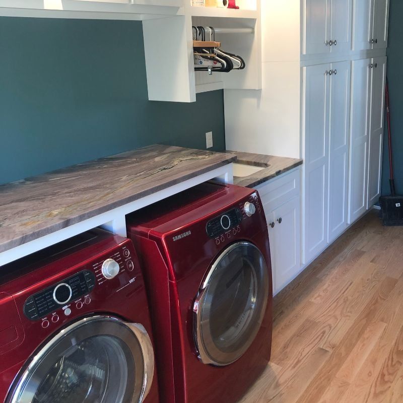 Red washer and dryer under a white countertop in a laundry room with blue walls and wood floor