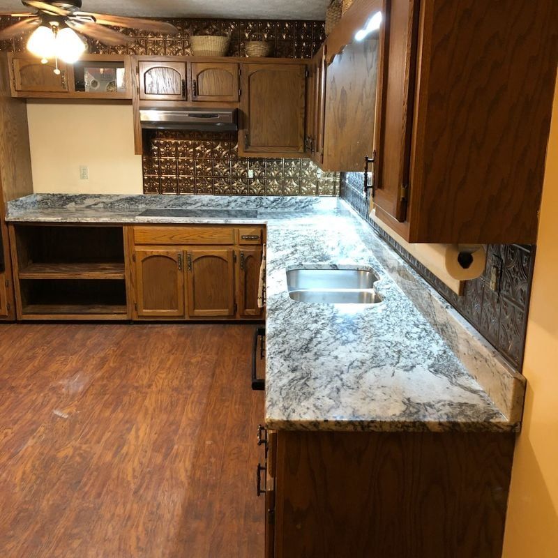 Empty kitchen with wood cabinets, speckled granite countertops, and a small sink area, viewed from one corner