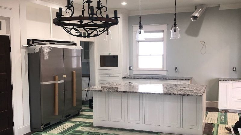 Modern kitchen with gray cabinets, granite island, chandelier, and stainless steel refrigerator