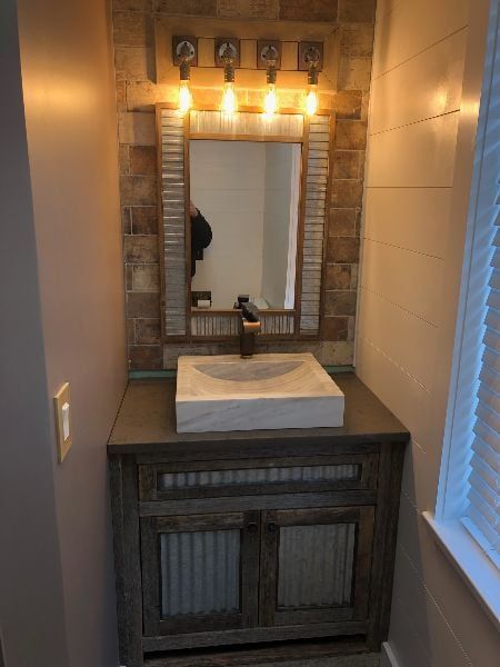 Bathroom vanity with mirror, vessel sink, and warm vanity lights between tiled walls