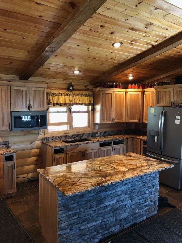 Rustic log cabin kitchen with stone island, wood ceiling, and stainless steel appliances