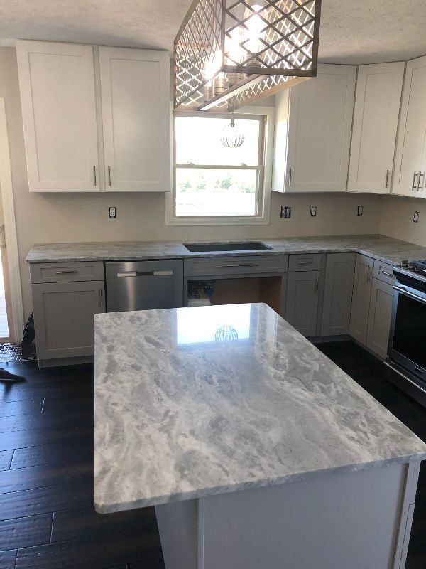 Bright kitchen with white cabinets, gray island countertop, and modern pendant light over dark floors.