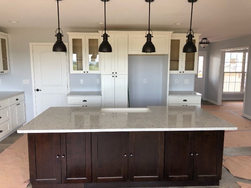 Modern kitchen with dark island, light countertops, pendant lights, and built-in cabinets