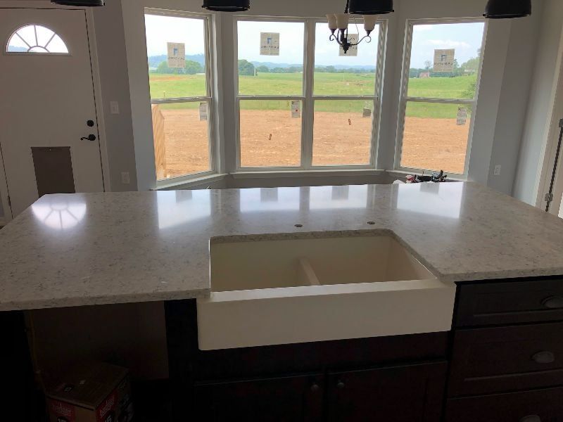 Kitchen island with white countertop and sink, facing large windows with a view of green fields