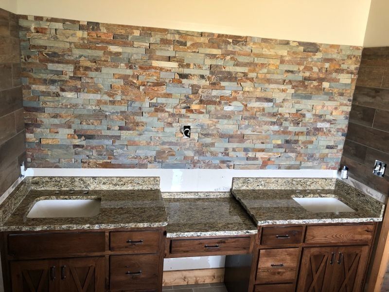 Kitchen counter with double sink, dark wood cabinets, and stone tile backsplash