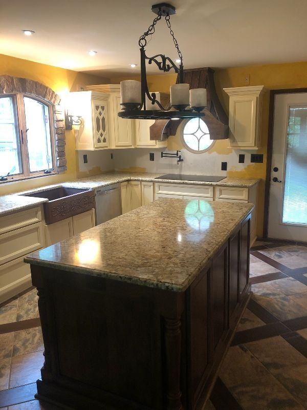 Spacious kitchen with granite island, white cabinets, arched window, and hanging chandelier.