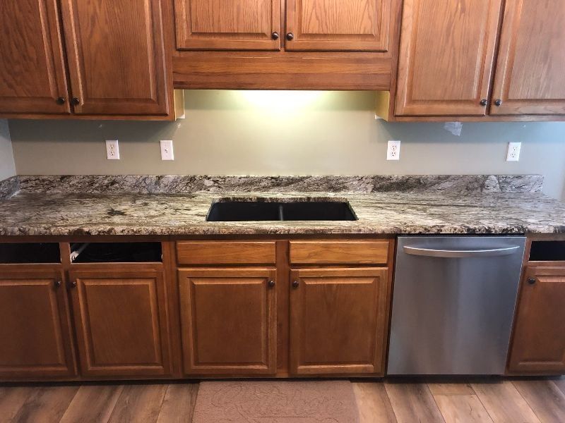 Kitchen counter with granite countertop, double sink cutout, wooden cabinets, and stainless dishwasher