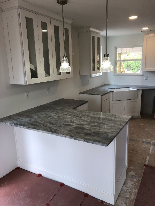 Kitchen with white cabinets, pendant lights, and dark stone countertops in an unfinished remodel