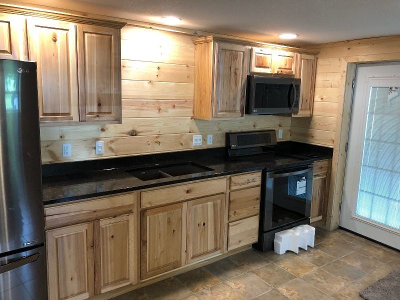 Wood-paneled kitchen with black countertops, stainless fridge, cabinets, stove, and glass door.