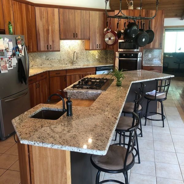 Modern kitchen with wood cabinets, granite island, hanging pots, and tiled floor.