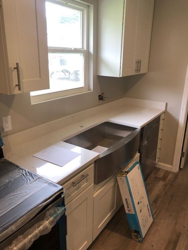 Kitchen under renovation with white cabinets, stainless sink area, and a window above the counter